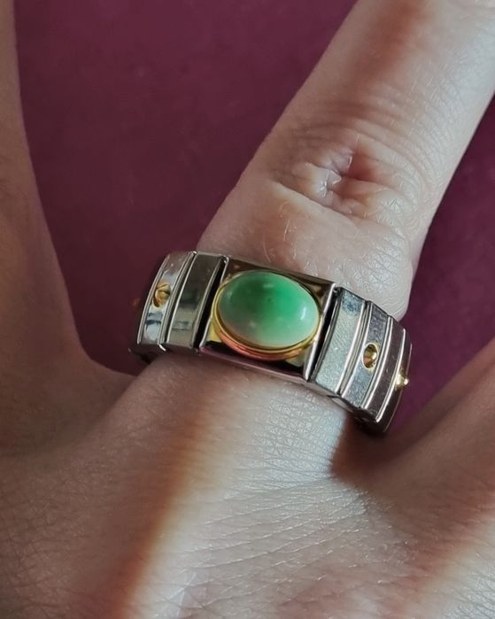 Anel prateado, em aço, com apontamentos dourados e pedrinha verde.