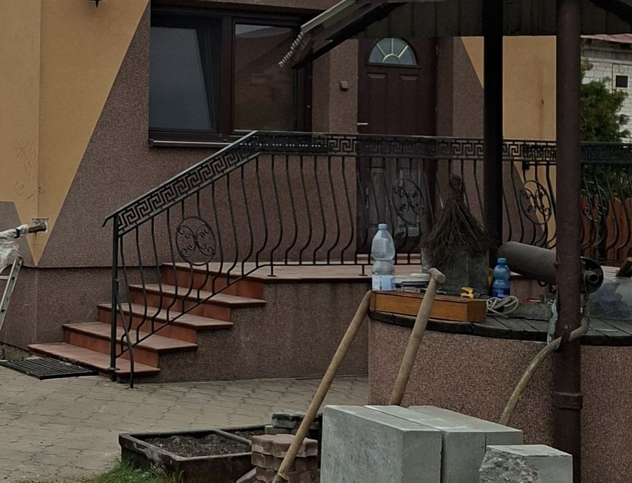 Solidna stalowa balustrada wykonana z grubych profili, z ozdobnym motywem greckim oraz dekoracyjnymi elementami kutymi