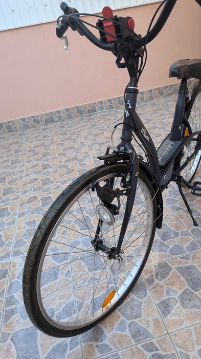 bicicleta  B'Twin Elops, apresentando um quadro de design urbano em preto.Modelo: B'Twin Elops 3 ou Elops 300. Inclui guarda-lamas e um selim preto.