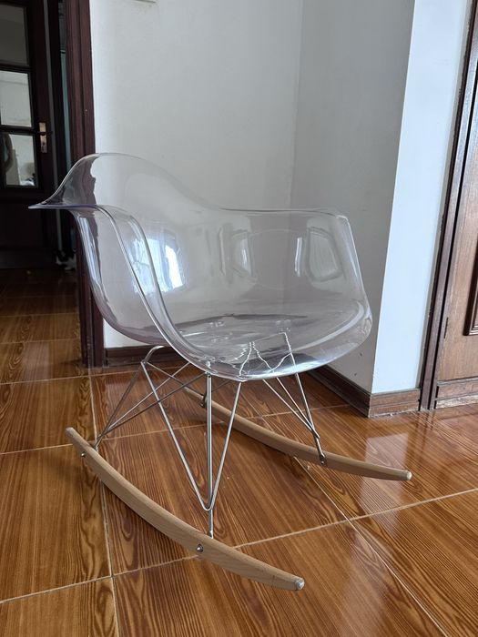 Cadeira de baloiço transparente, que se destaca pelo seu assento translúcido em acrílico combinado com pés de madeira em forma de baloiço