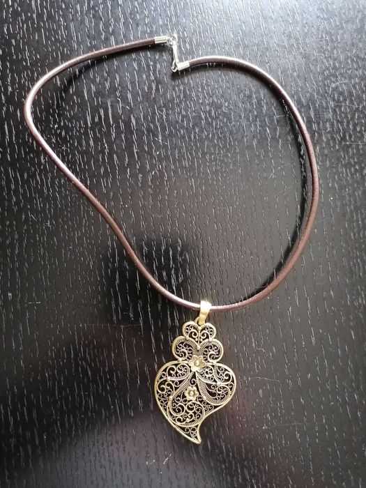 Fio em couro com pendente de coração de Viana em metal amarelo.