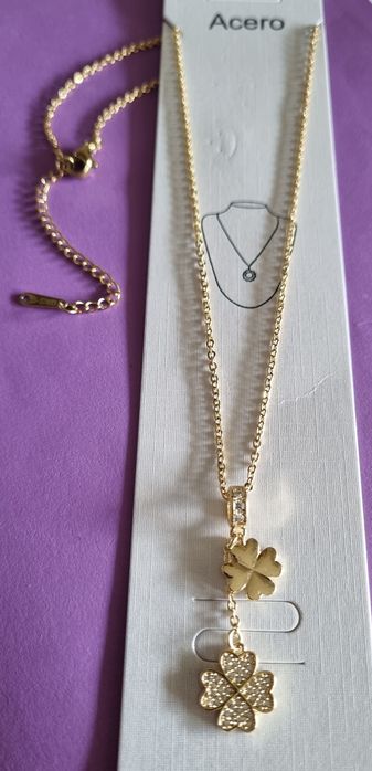 Colar dourado, em aço, com 2 trevos pendentes. Formato gravata.