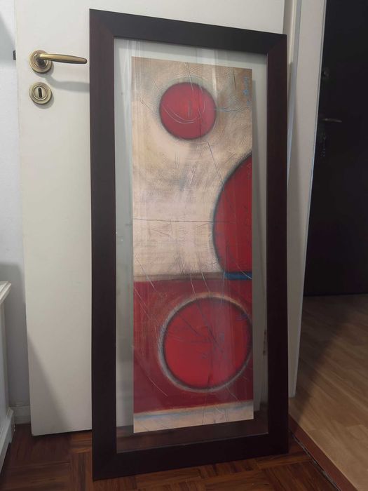 Quadro decorativo, com figuras geométricas em tons de vermelho e moldura de madeira castanha escura.