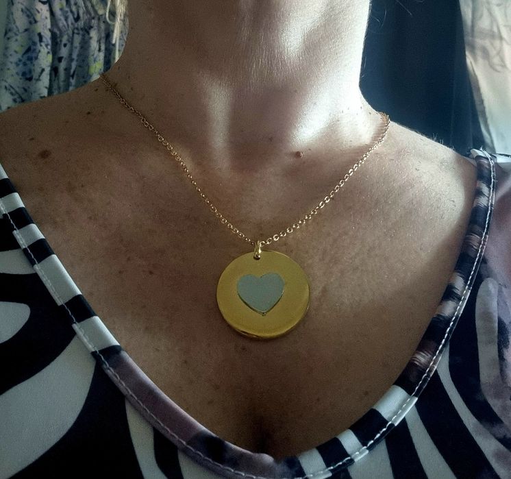 Colar dourado, em aço, com pingente redondo dourado e um coração prateado no centro