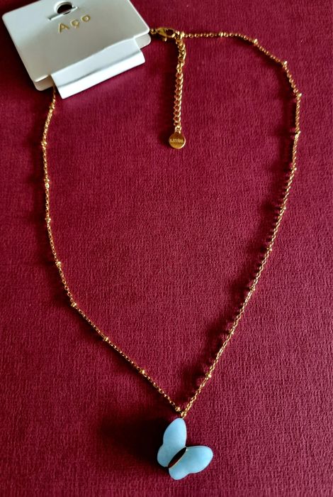 Colar dourado, em aço, malha com bolinhas e pingente borboleta azul.