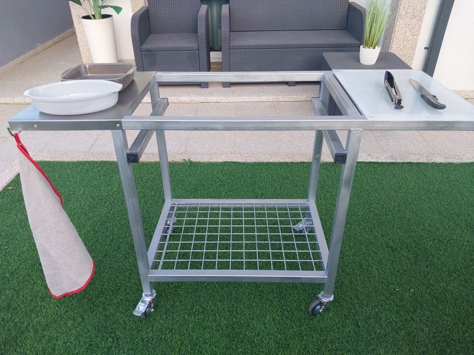 Churrasqueira com rodas, tem queimador  e grelha em inox  duas mesas de apoio uma em inox outra em nylon  e plataforma para lenha..