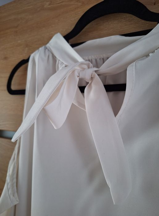 Biała bluzka z wycięciem na ramiona i ozdobnym wiązaniem na tyle