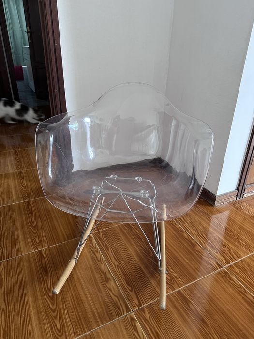 Cadeira de baloiço transparente, que se destaca pelo seu assento translúcido em acrílico combinado com pés de madeira em forma de baloiço