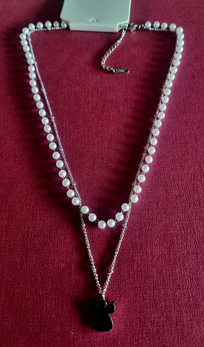 Colar duplo, em aço, 1 de pérolas e 1 com anjinho. Tem extensor