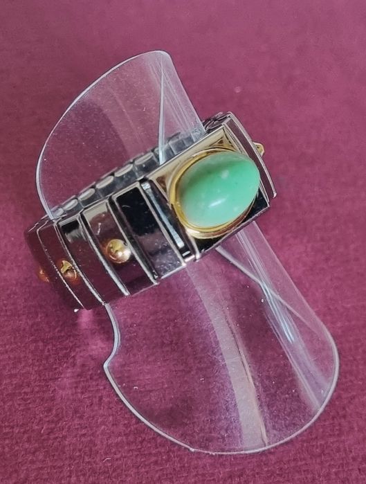 Anel prateado, em aço, com apontamentos dourados e pedrinha verde.
