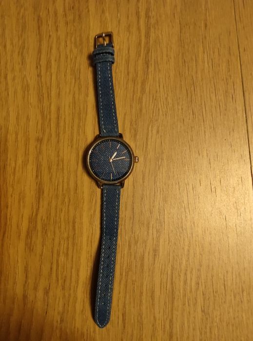Zegarek damski marki Reserved posiada kopertę w kolorze złotym oraz pasek wykonany z materiału imitującego dżins.Model: OR081-59X.