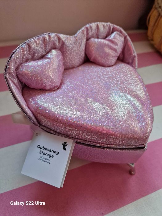 Pequena caixa de joias em forma de cama, de cor rosa.