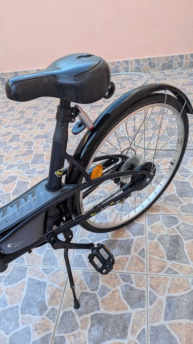 bicicleta  B'Twin Elops, apresentando um quadro de design urbano em preto.Modelo: B'Twin Elops 3 ou Elops 300. Inclui guarda-lamas e um selim preto.