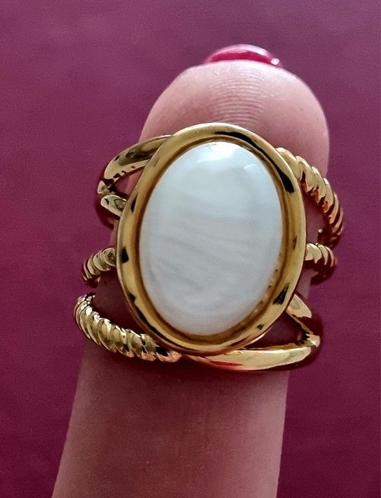 Anel dourado, em aço, com uma  madrepérola  oval no centro. Ajustável