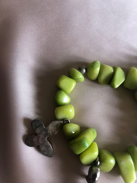 Pulseira com pedras verdes e elementos metálicos como o trevo e outros