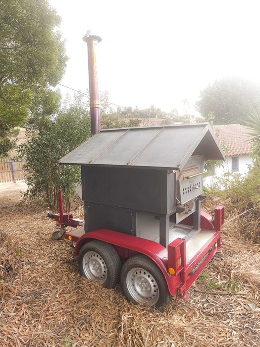Forno de pedra a lenha profissional e móvel, montado sobre um chassis de reboque, concebido para eventos e utilização comercial em pequena escala.