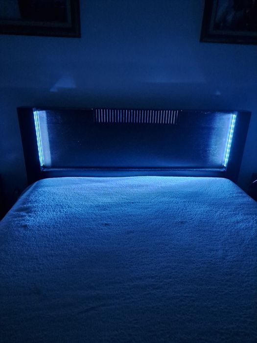 Cama de casal,  cor castanho escuro, com iluminação.