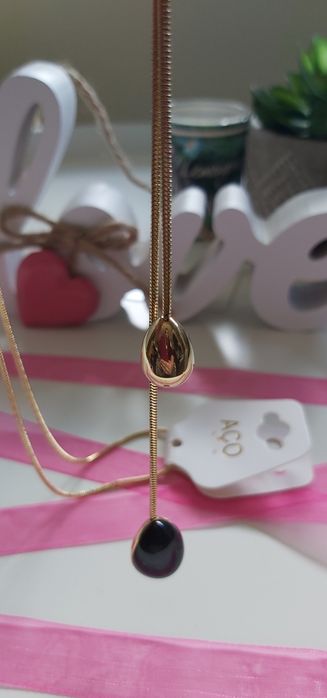 Colar dourado, em aço, com pedra preta. Estilo gravata