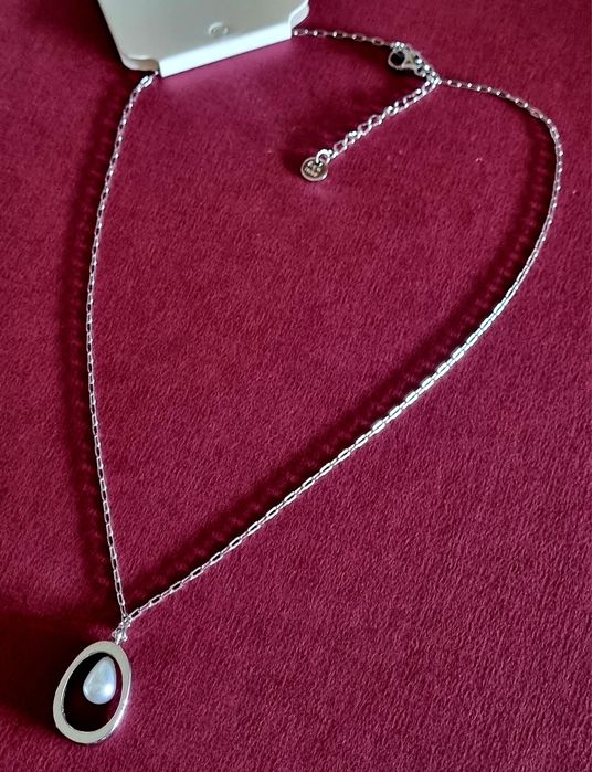 Colar prateado, em aço, com pingente oval e 1 pérola no centro. Tem extensor