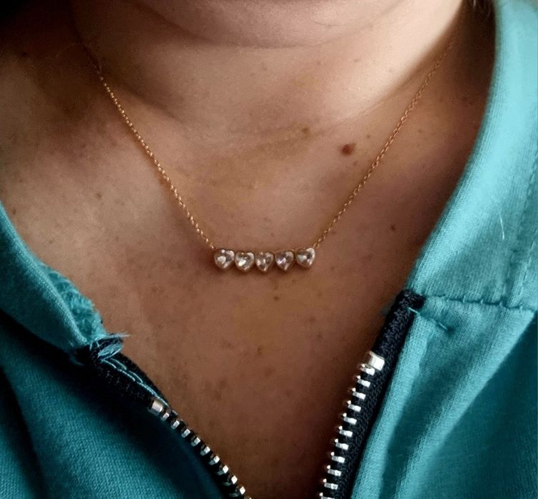 Colar dourado, em aço, com 5 pequenos corações em pedra de vidro.