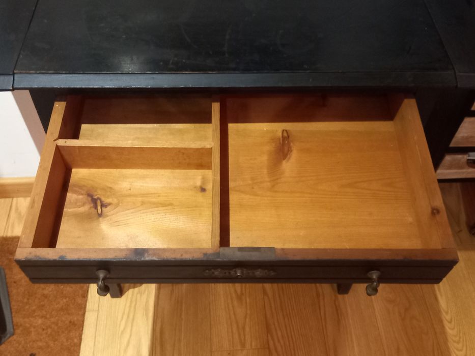 Mesa de apoio preta, antiga. Tem 2 abas pequenas e uma gaveta.