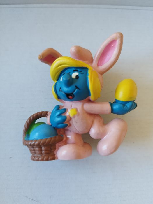 Smurfina vestida de coelhinha cor-de-rosa com um cesto e um ovo de Pás
