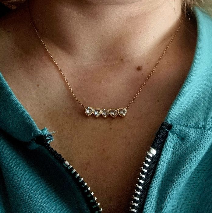 Colar dourado, em aço, com 5 pequenos corações em pedra de vidro.