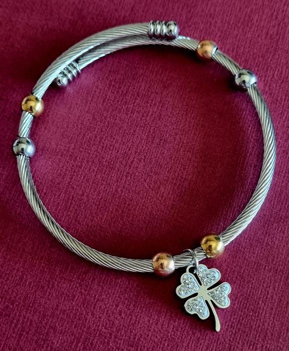 Pulseira prateada, em aço, com bolinhas douradas e um trevo da sorte.