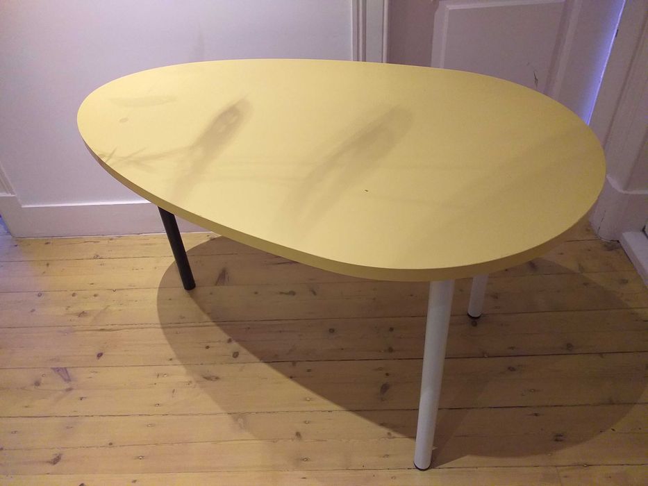 Mesa design oval com cor amarela, uso versátil.