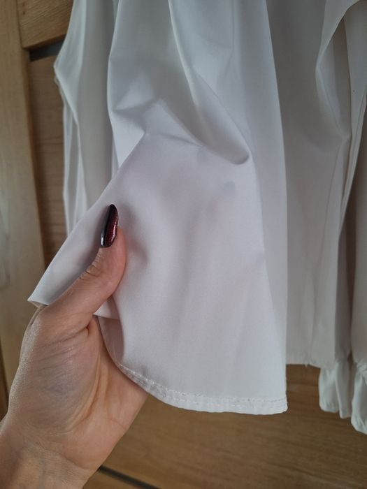 Biała bluzka z wycięciem na ramiona i ozdobnym wiązaniem na tyle