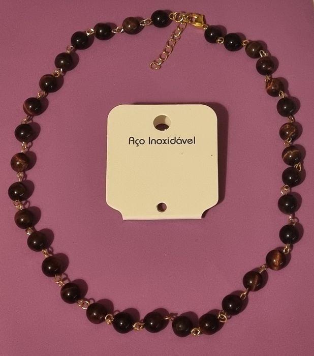 Colar dourado, em aço, às bolinhas castanhas de pedra natural "olho de gato". Tem extensor.