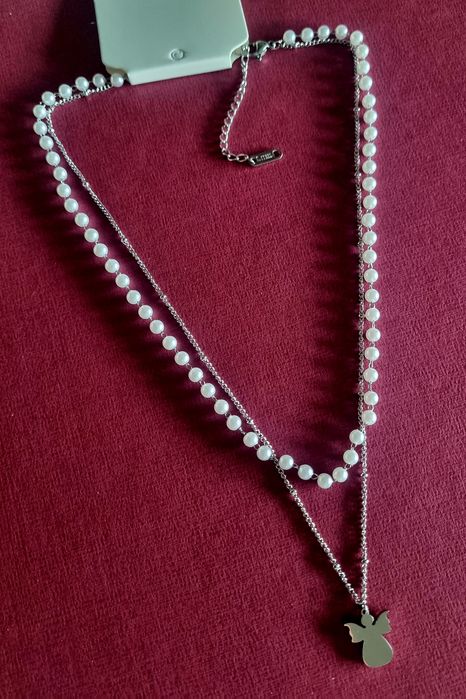Colar duplo, em aço, 1 de pérolas e 1 com anjinho. Tem extensor
