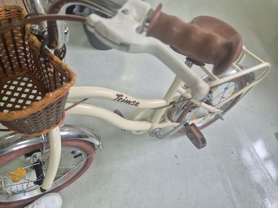 Bicicleta infantil de estilo vintage cor creme/bege com selim e punhos castanhos, acompanhada de um cesto de vime