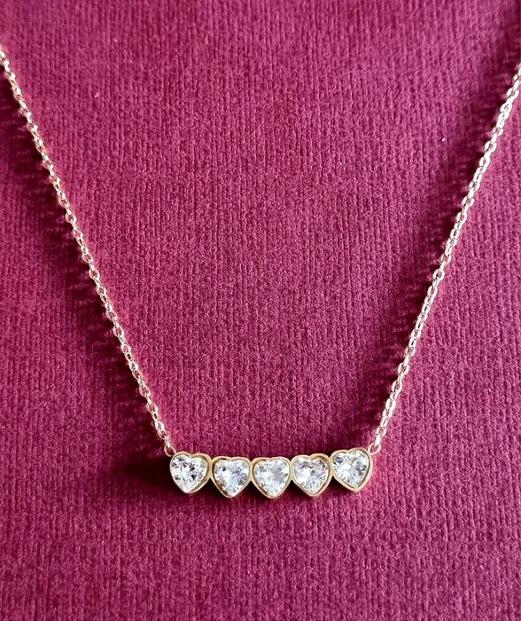 Colar dourado, em aço, com 5 pequenos corações em pedra de vidro.