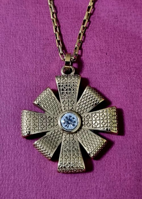 Colar dourado, em aço, com flor trabalhada e um ponto de luz central.