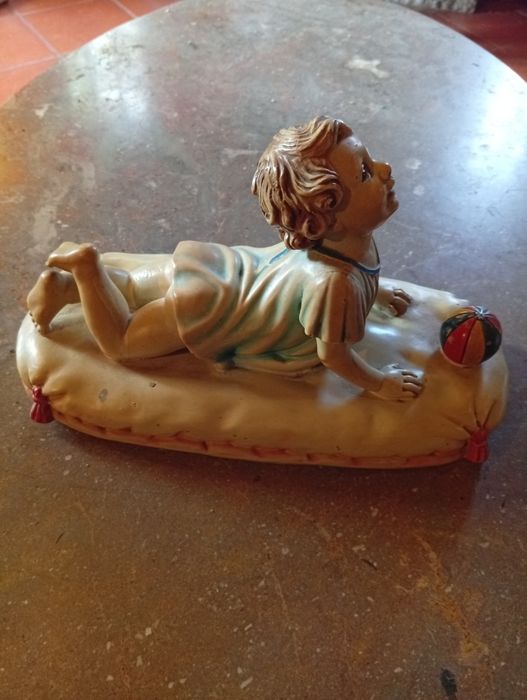 Figura cerâmica de bebé sobre uma almofada com uma bola