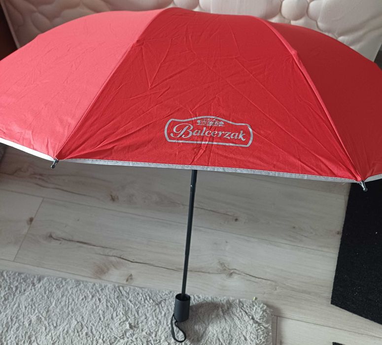 Parasol składany. Ten czerwony parasol jest oznaczony logo polskiej firmy mięsnej Balcerzak.
