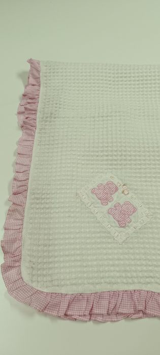 Manta de criança branca com folho e bonecos em cor de rosa . Tem umas