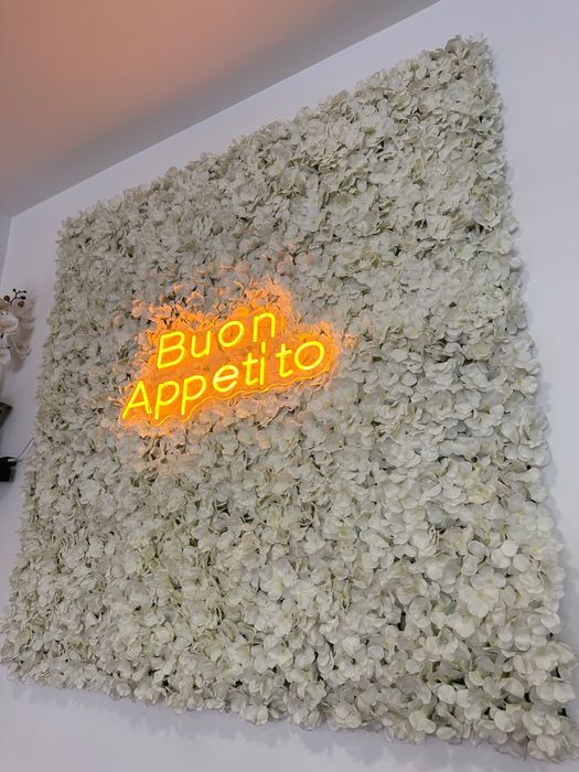 Painel decorativo com flores artificiais e letreiro luminoso “Buon Appetito”