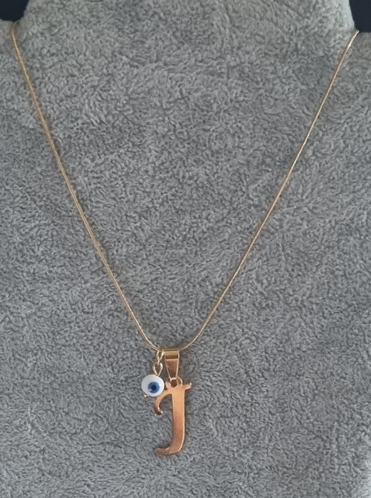 Colar dourado, em aço, com a letra "J" e olho turco. Tem extensor