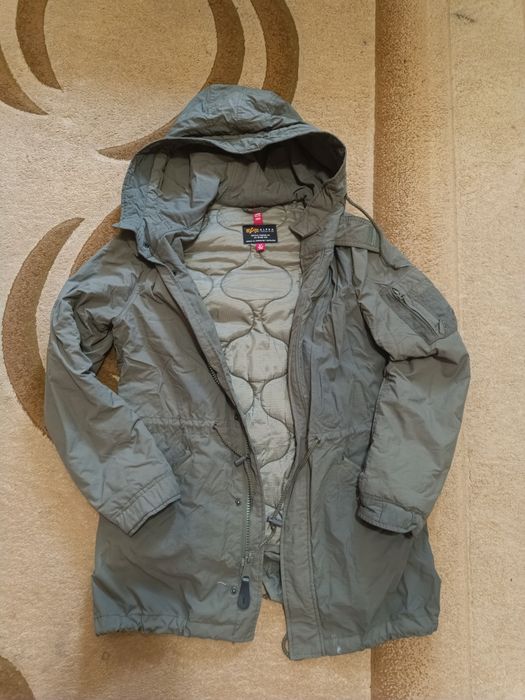 Продам оливково-зелену куртку-парку з капюшоном від бренду Alpha Industries, яка має світлу стьобану підкладку та характерний фіриовий лейб