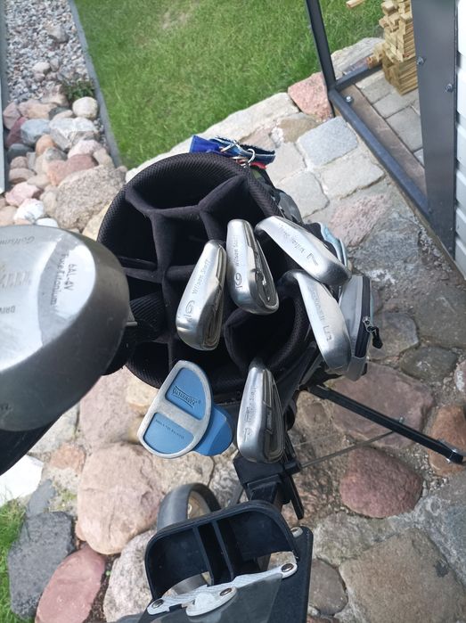 Zestaw kijów golfowych wraz z torbą i wózkiem.