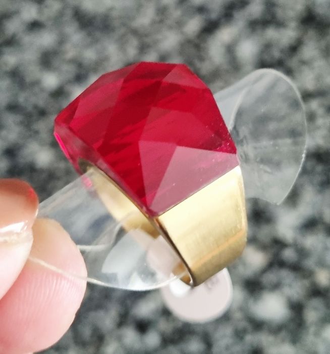 Anel dourado, em aço, com vermelho facetado na parte de cima. T17