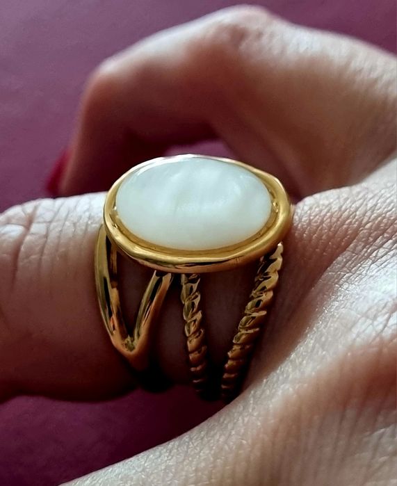 Anel dourado, em aço, com uma  madrepérola  oval no centro. Ajustável
