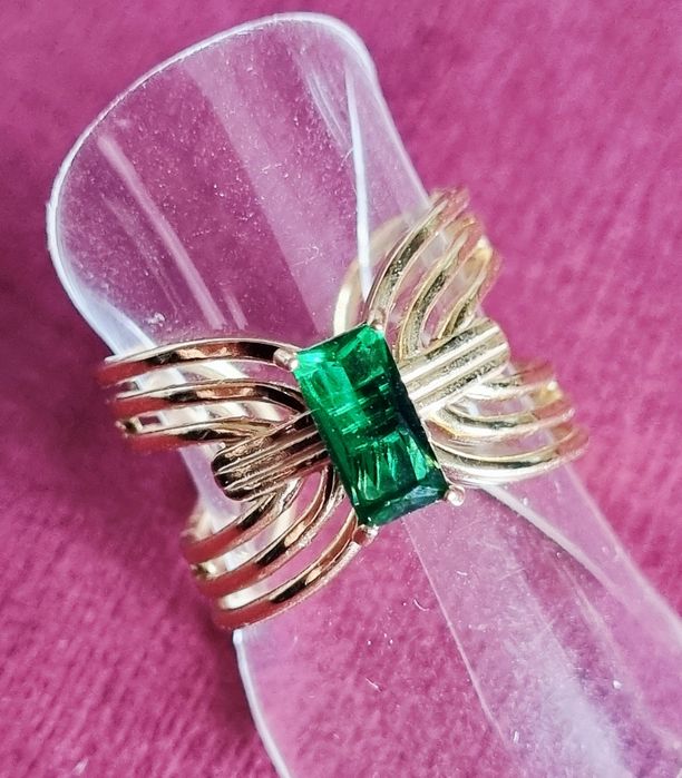 Anel dourado, em aço, com pedrinha retangular verde no centro. Ajustável