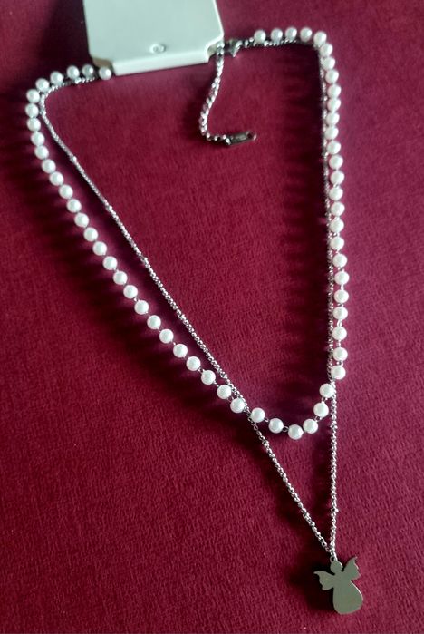 Colar duplo, em aço, 1 de pérolas e 1 com anjinho. Tem extensor