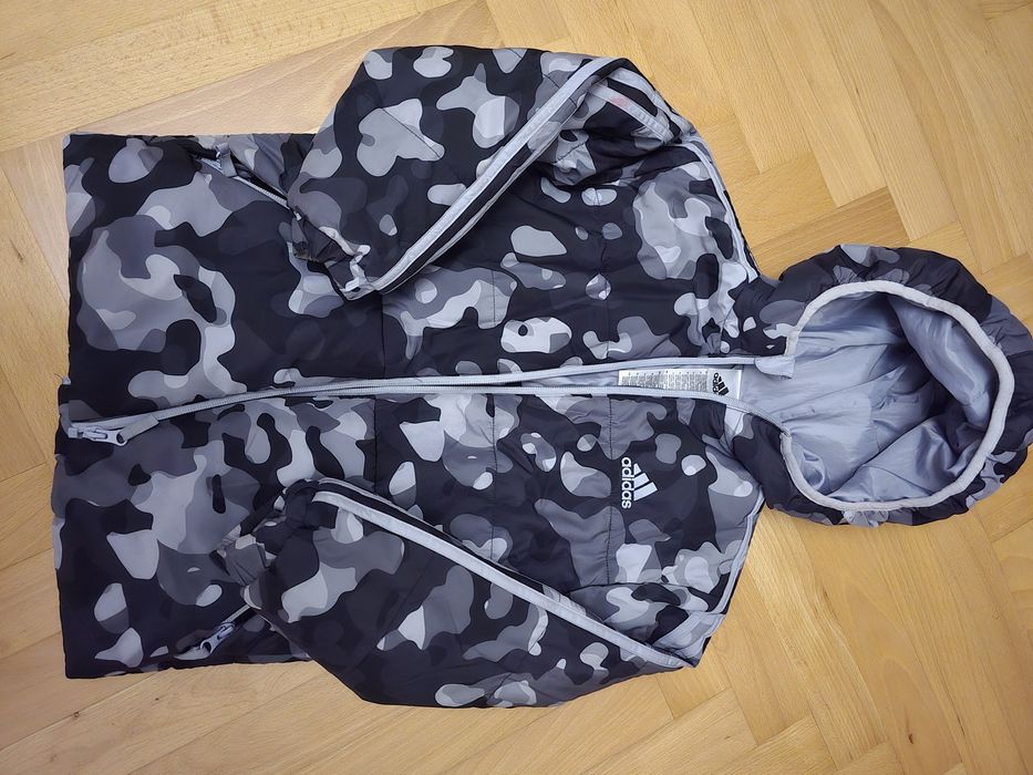 дитяча куртка Adidas має сірий камуфляжний принт.Бренд: Adidas.Дизайн: Сірий камуфляжний візерунок ("Camo Allover Print").