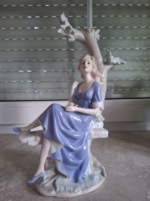 Piękna porcelanowa figurka dziewczyna siedząca na drzewie