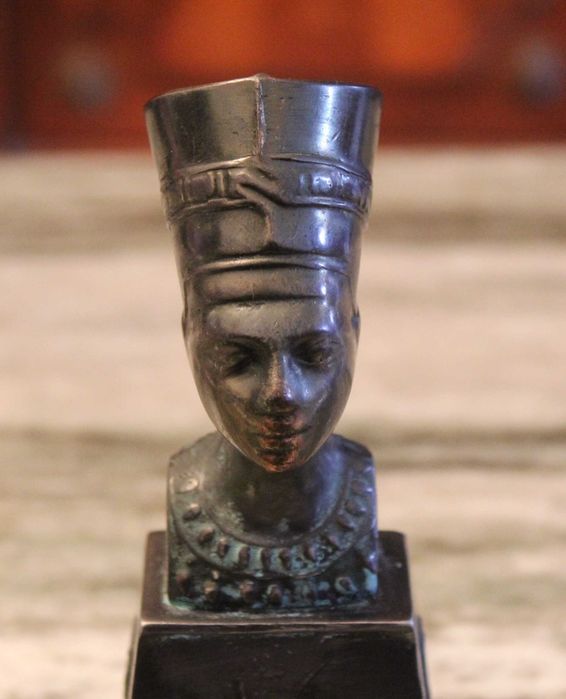 Busto de Nefertiti com 15,5cm de altura em metal sobre madeira.