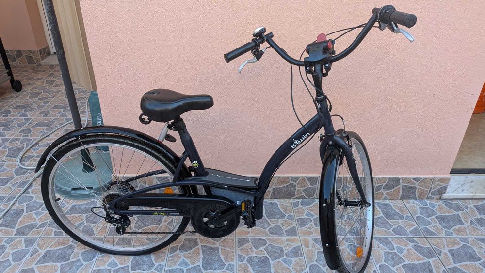 bicicleta  B'Twin Elops, apresentando um quadro de design urbano em preto.Modelo: B'Twin Elops 3 ou Elops 300. Inclui guarda-lamas e um selim preto.